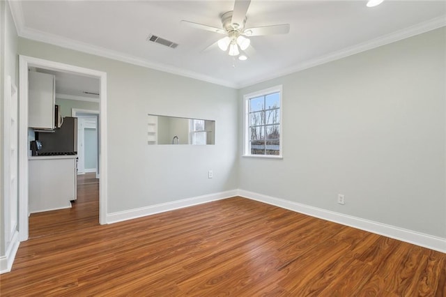 empty room with baseboards, visible vents, ceiling fan, wood finished floors, and crown molding