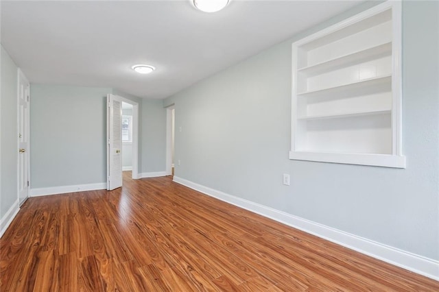 spare room featuring built in shelves, baseboards, and wood finished floors