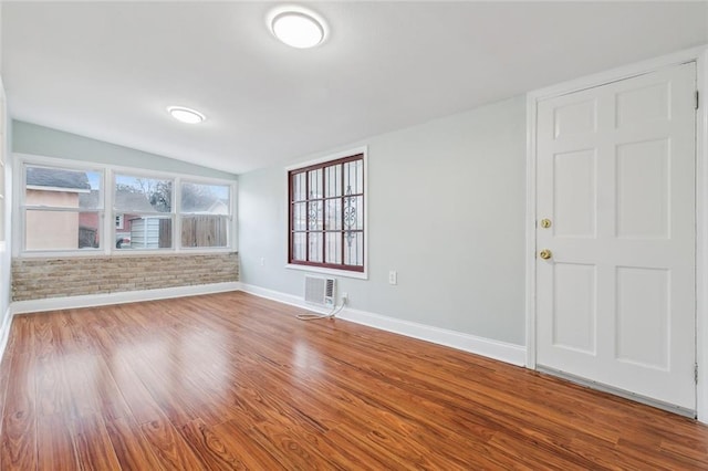 empty room with lofted ceiling, brick wall, baseboards, and wood finished floors