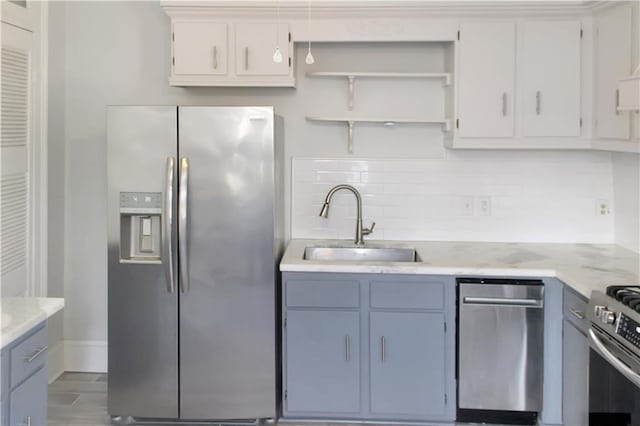 kitchen featuring light stone counters, a sink, appliances with stainless steel finishes, backsplash, and open shelves