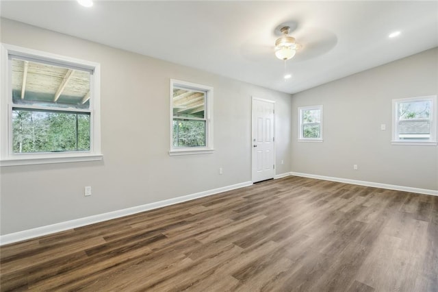 spare room with lofted ceiling, dark wood-type flooring, baseboards, and a healthy amount of sunlight