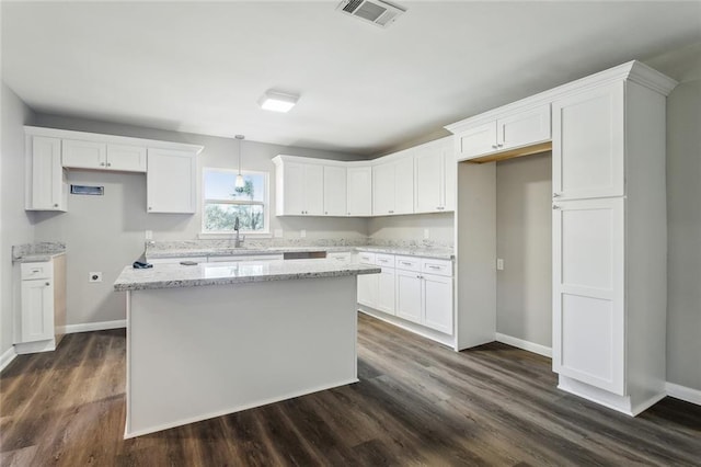 kitchen with visible vents, light stone countertops, white cabinetry, and a center island