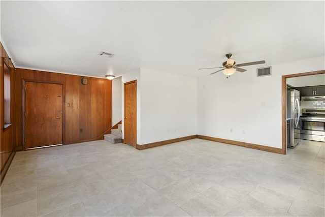 spare room with stairway, visible vents, a ceiling fan, and wood walls