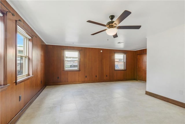 empty room with baseboards, visible vents, a wealth of natural light, and wooden walls