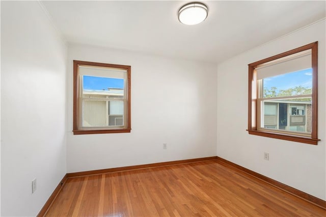 empty room featuring light wood finished floors, baseboards, and ornamental molding
