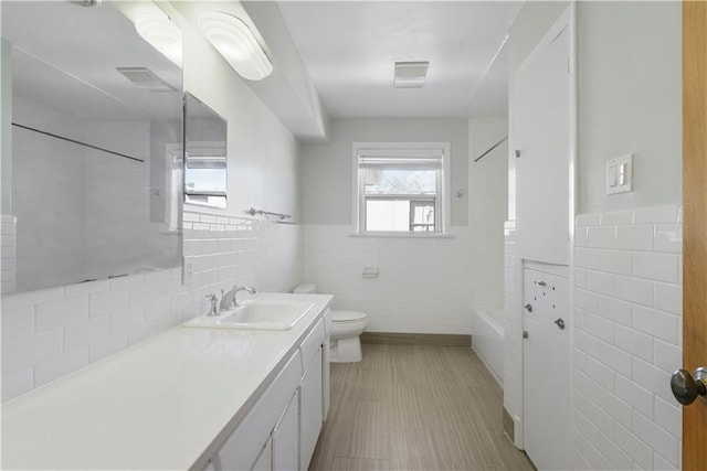 bathroom featuring toilet, visible vents, vanity, and tile walls
