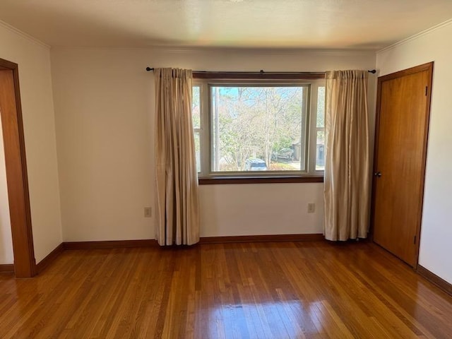 spare room with baseboards, wood finished floors, and ornamental molding