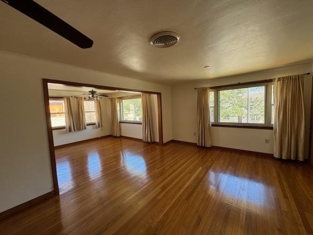 empty room with dark wood-style flooring, visible vents, and baseboards