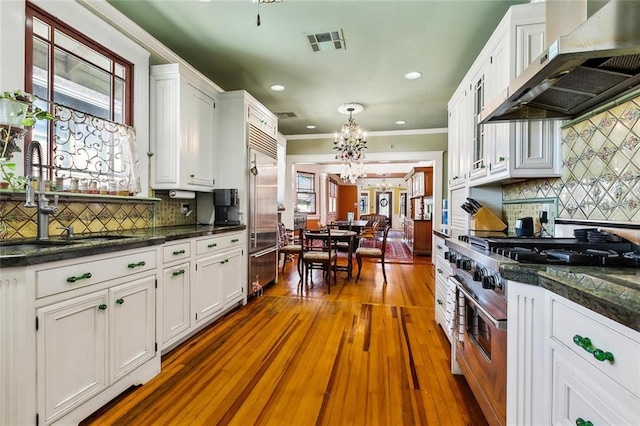 kitchen featuring a chandelier, premium appliances, visible vents, white cabinets, and wall chimney exhaust hood