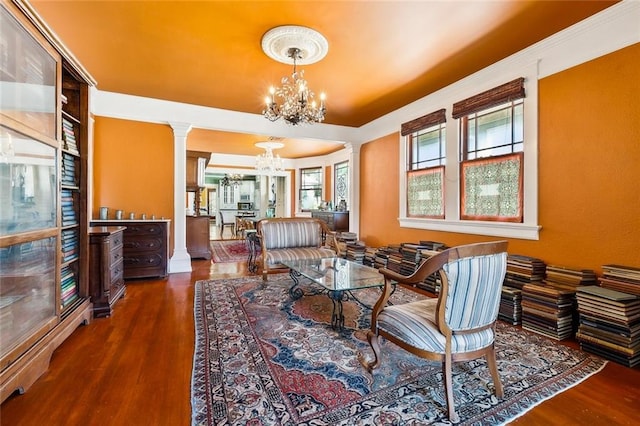 living area featuring a chandelier, dark wood-type flooring, and ornate columns