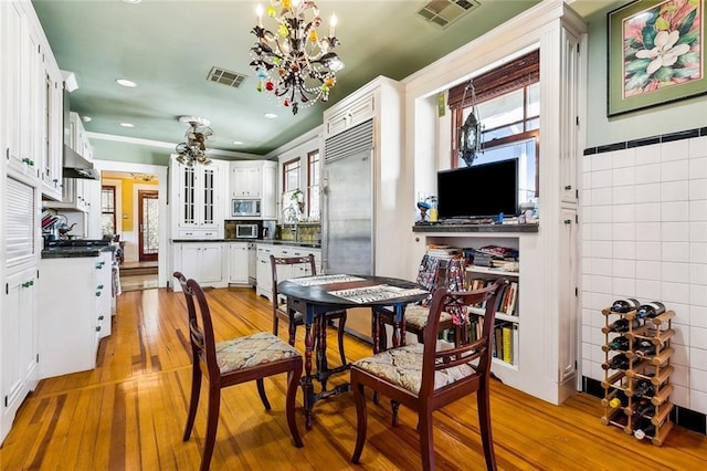 dining area with an inviting chandelier, tile walls, visible vents, and light wood-style floors