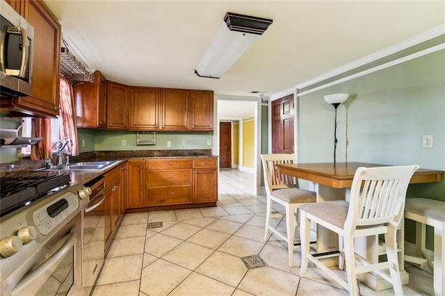 kitchen featuring stainless steel appliances, brown cabinetry, dark countertops, and a sink