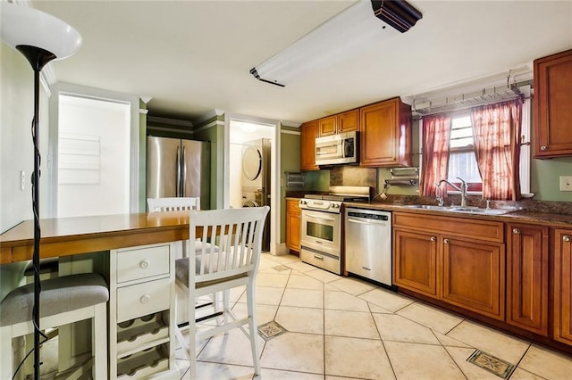 kitchen featuring light tile patterned floors, brown cabinetry, dark countertops, stainless steel appliances, and a sink