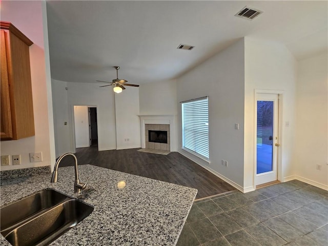 kitchen featuring visible vents, light stone counters, a sink, and a tile fireplace