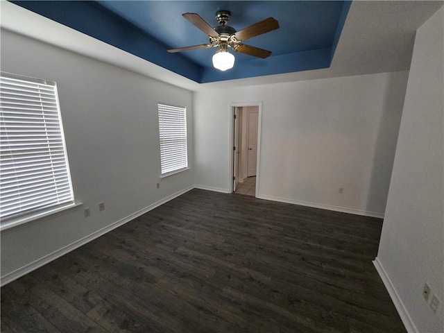 spare room featuring dark wood-style floors, ceiling fan, baseboards, and a raised ceiling