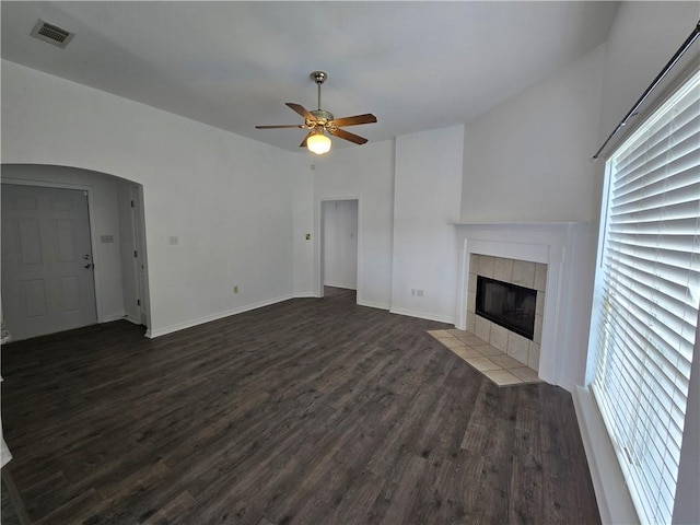 unfurnished living room with arched walkways, dark wood-style flooring, visible vents, baseboards, and a tiled fireplace