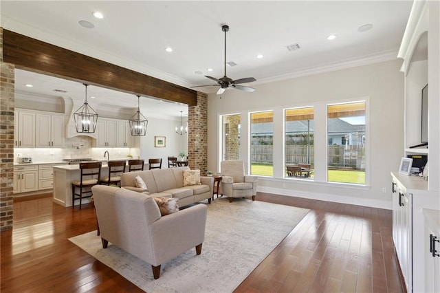 living room with dark wood-style flooring, recessed lighting, visible vents, ornamental molding, and ceiling fan with notable chandelier