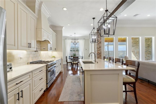 kitchen with a center island with sink, a kitchen breakfast bar, decorative light fixtures, high end stainless steel range oven, and light countertops