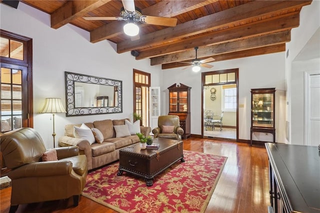 living area with beam ceiling, a ceiling fan, wood finished floors, wooden ceiling, and baseboards