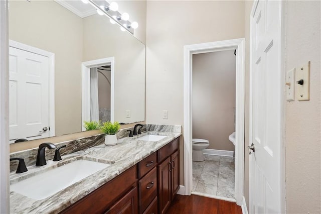 full bath featuring double vanity, a sink, toilet, and baseboards