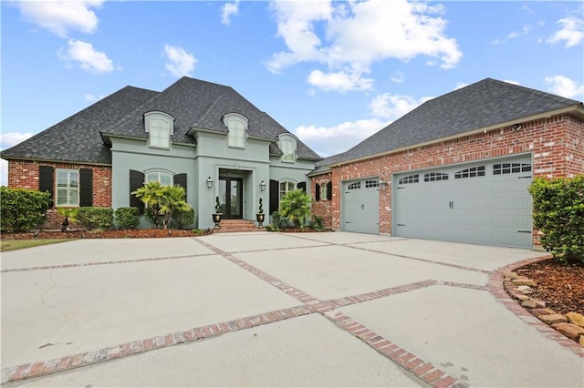 french country style house with driveway, brick siding, a garage, and roof with shingles