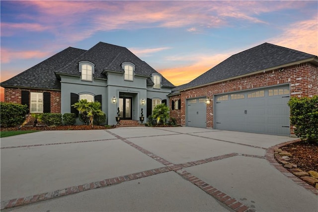 french provincial home with brick siding, concrete driveway, a garage, and roof with shingles