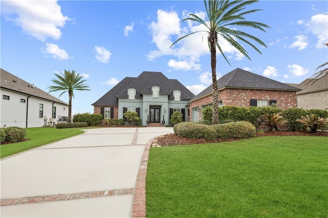 french country style house featuring an attached garage, a front lawn, concrete driveway, and brick siding