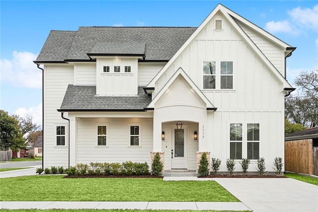 modern farmhouse featuring roof with shingles, board and batten siding, fence, and a front lawn