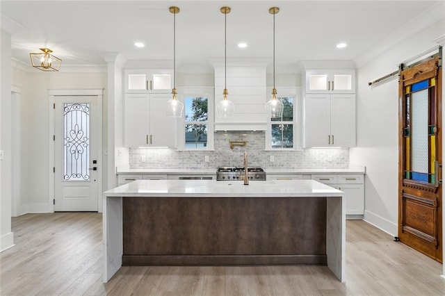 kitchen with range, white cabinetry, light countertops, a center island with sink, and decorative backsplash