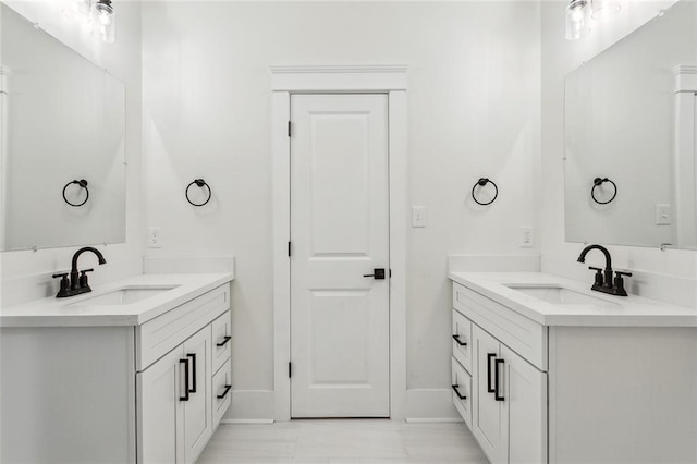 full bath featuring two vanities, baseboards, and a sink
