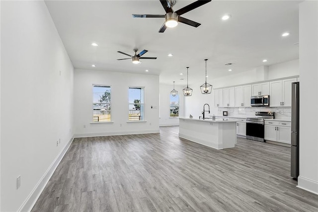 kitchen with a center island with sink, white cabinets, open floor plan, stainless steel appliances, and light countertops