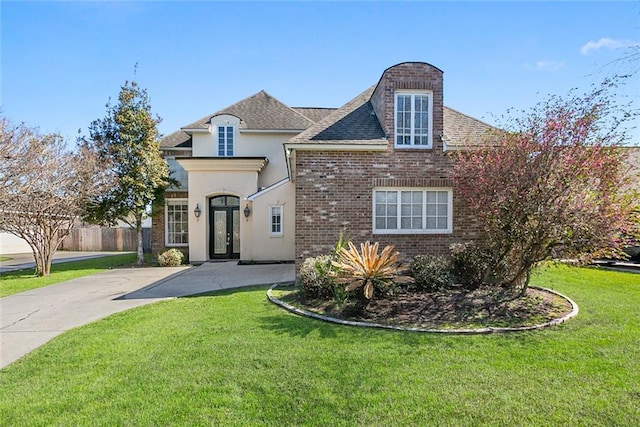 french country home with brick siding, fence, french doors, roof with shingles, and a front yard