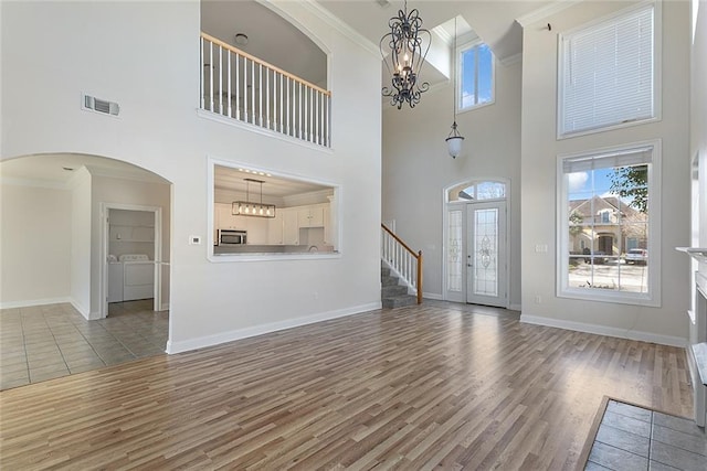 unfurnished living room with a chandelier, separate washer and dryer, visible vents, and crown molding