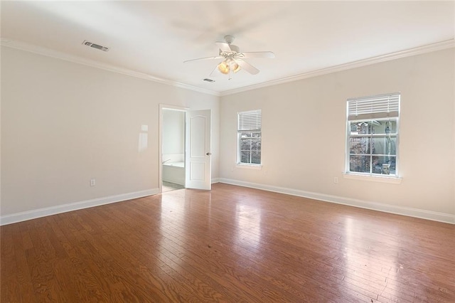 empty room featuring ornamental molding, wood finished floors, a wealth of natural light, and baseboards