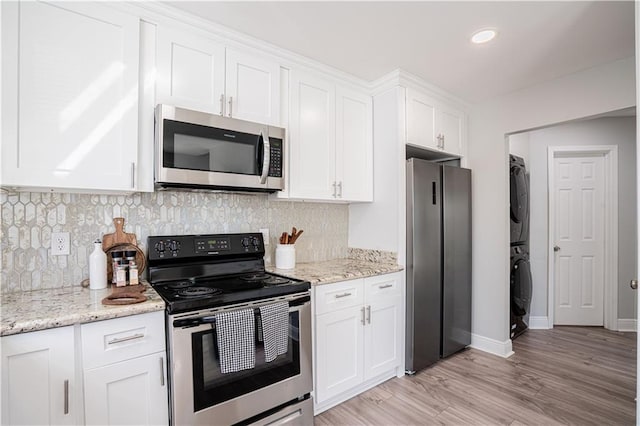 kitchen with light stone counters, tasteful backsplash, stacked washer / drying machine, appliances with stainless steel finishes, and white cabinets