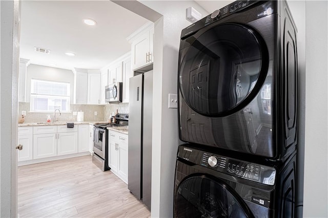 laundry area featuring stacked washer and dryer, laundry area, visible vents, light wood-type flooring, and a sink