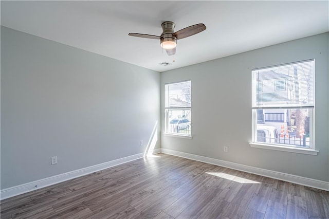 spare room featuring a ceiling fan, visible vents, baseboards, and wood finished floors