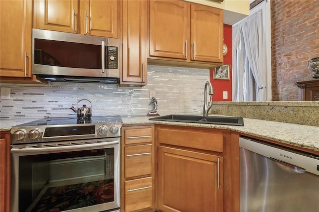 kitchen featuring stainless steel appliances, brown cabinets, a sink, and light stone countertops