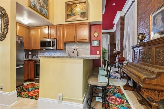 kitchen featuring light tile patterned floors, stainless steel appliances, a sink, tasteful backsplash, and a kitchen bar