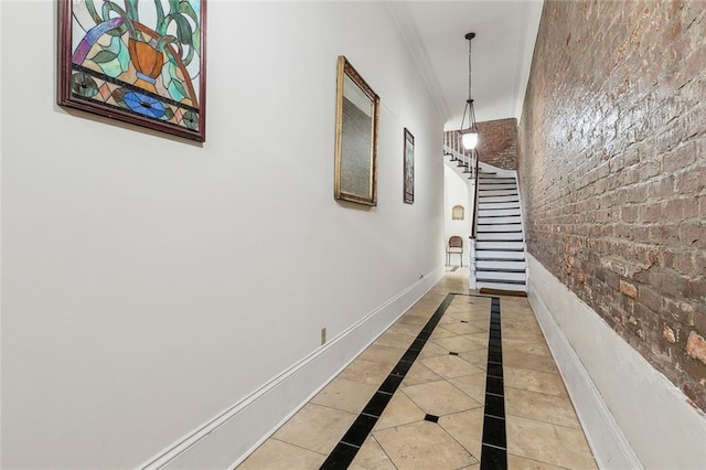 hallway featuring light tile patterned floors, brick wall, stairs, and baseboards