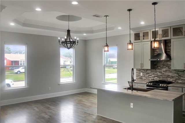 kitchen featuring gas range oven, a raised ceiling, glass insert cabinets, wall chimney range hood, and light stone countertops