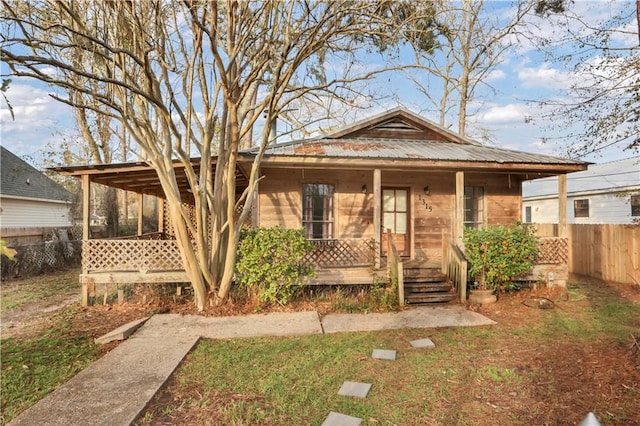 bungalow with covered porch, fence, and metal roof