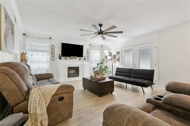 living room with french doors, crown molding, a fireplace, light wood-style flooring, and ceiling fan