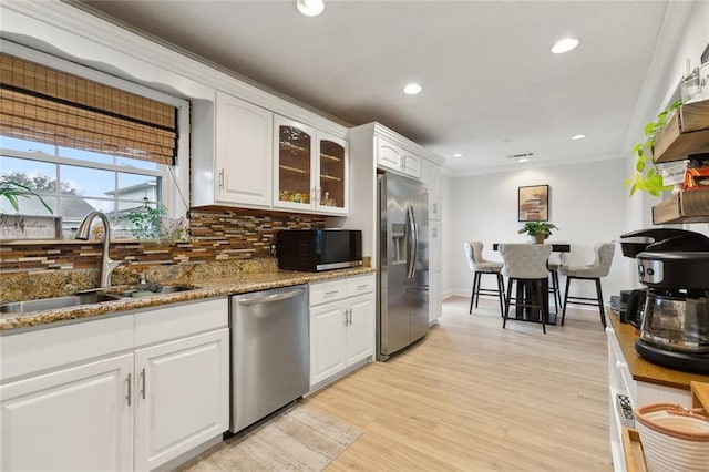 kitchen featuring stone countertops, glass insert cabinets, stainless steel appliances, white cabinetry, and a sink