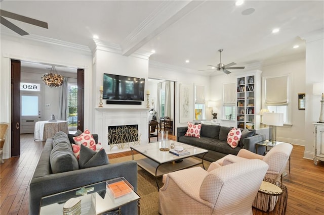 living room featuring baseboards, ornamental molding, wood finished floors, a fireplace, and ceiling fan with notable chandelier