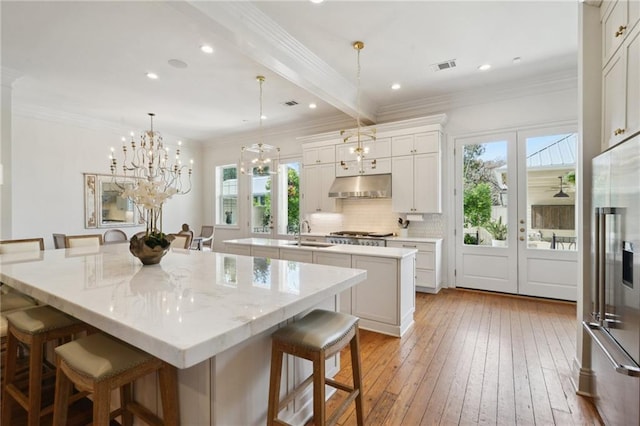 kitchen with a spacious island, a breakfast bar, white cabinets, and under cabinet range hood