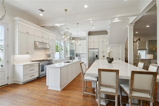 kitchen featuring pendant lighting, light countertops, a kitchen island with sink, high quality appliances, and under cabinet range hood