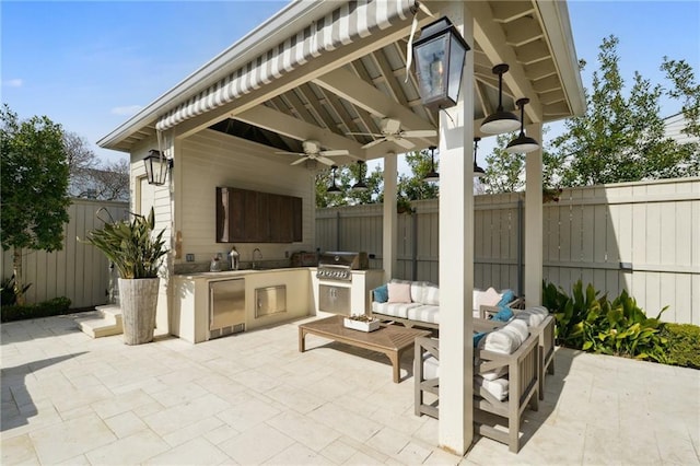 view of patio featuring a ceiling fan, a fenced backyard, grilling area, exterior kitchen, and outdoor lounge area