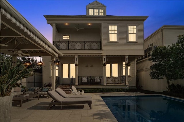 back of house at dusk featuring a fenced in pool, a patio, fence, ceiling fan, and a balcony