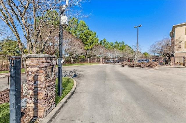 view of road featuring street lighting, a gate, a gated entry, and curbs